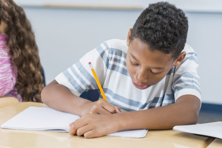 Boy sitting at desk in class writing in notebook | NNPA ESSA MEDIA CAMPAIGN