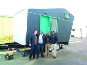 Truck driver Martin Kauffman (far left) and electrician Art Ramirez (far right), who both donated their services to deliver Laney College’s tiny home prototype to West Side Missionary Baptist Church, stand in front of the Pocket House Model M with Rev. Ken Chambers (middle right) and Councilmember Abel Guillén (middle left).