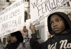 Talks around details on language in the George Floyd Justice in Policing Act in Congress ended in late September after a dispute between Republican Senator Tim Scott (R-SC) over what Scott defined as “defunding police.” (Photo: Philadelphia, PA USA - November 24, 2014; A young protester and his mother are seen holding signs at Dillworth Park at Philadelphia City Hall. [photo by Bas Slabbers] / iStockphoto / NNPA)