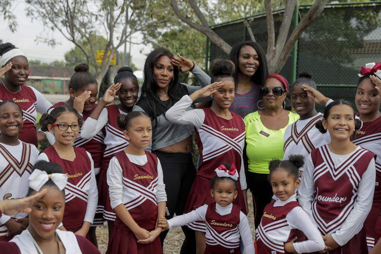 FILE - Serena Williams, center left, and sister, Venus, pose with the members of the Compton Sounders drill team after attending a dedication ceremony of the Lueders Park tennis courts Saturday, Nov. 12, 2016, in Compton, Calif. The courts were dedicated in their name. After nearly three decades in the public eye, few can match Serena Williams' array of accomplishments, medals and awards. Through it all, the 23-time Grand Slam title winner hasn't let the public forget that she's a Black American woman who embraces her responsibility as a beacon for her people. (AP Photo/Jae C. Hong, File)