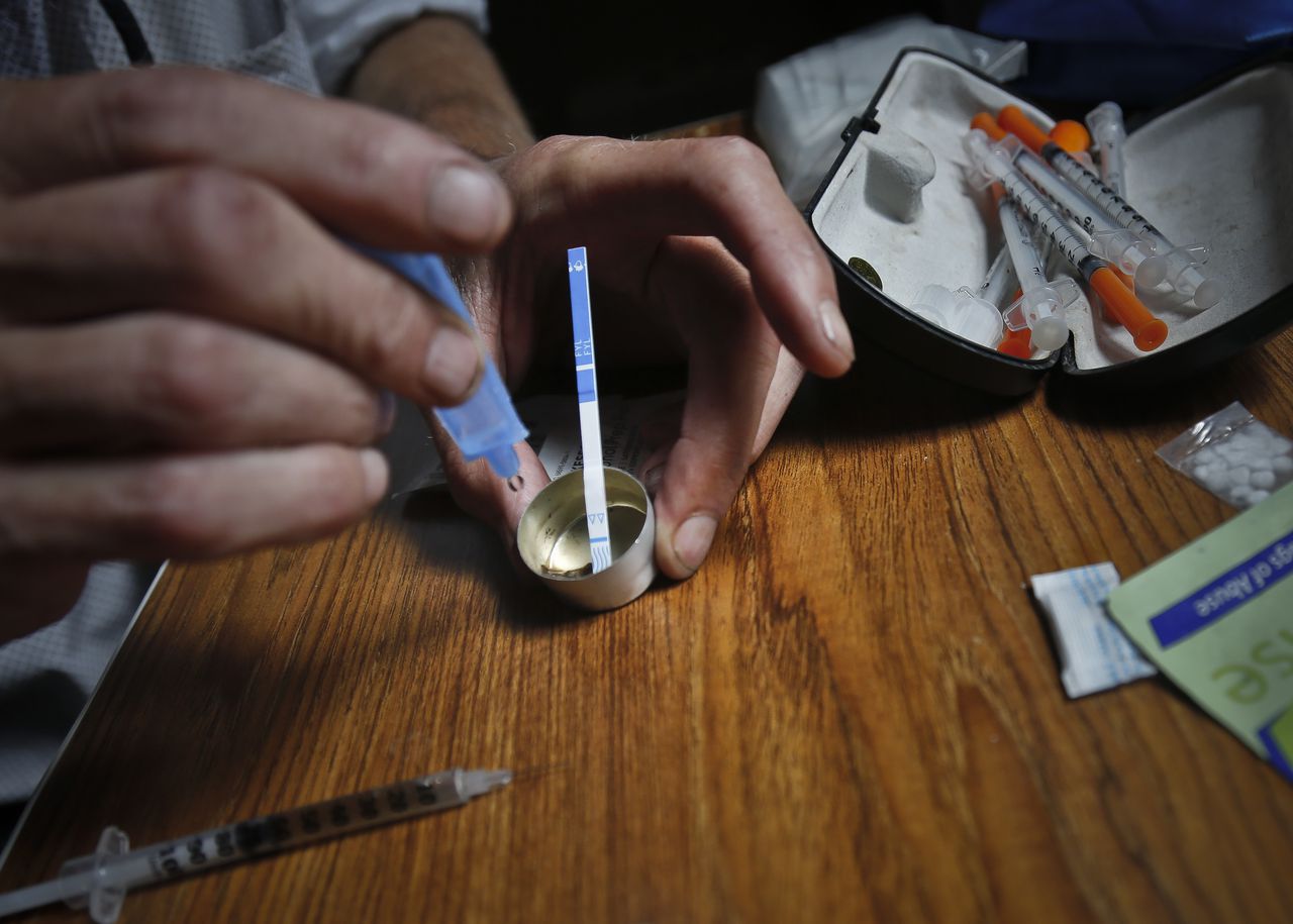 An addict prepares heroin, placing a fentanyl test strip into the mixing container to check for contamination