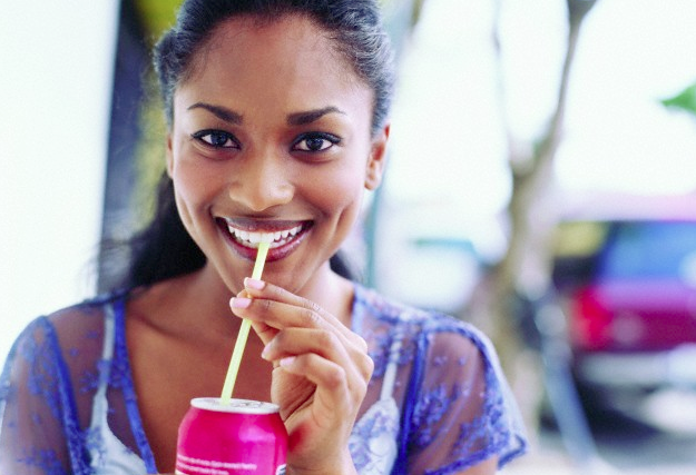 A woman drinking from a soda can with a straw